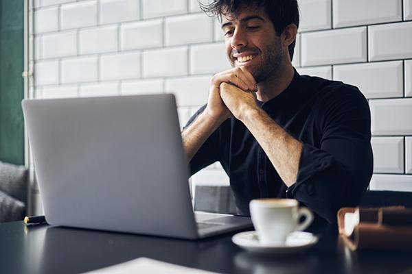一个男人微笑着坐在笔记本电脑前，旁边放着一个杯子.